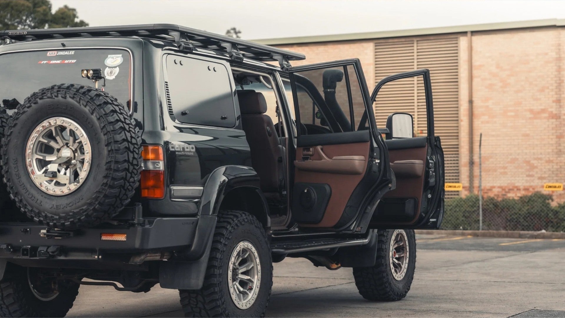 Black 80 Series LandCruiser with its doors open, showing a brown leather interior